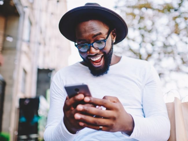 Un homme heureux de l'arrivée de la 5G à Paris rit devant son smartphone.