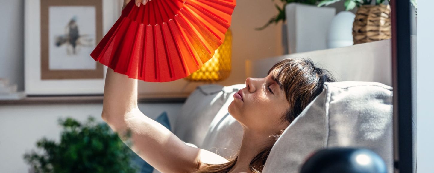 Une femme se ventile avec un éventail car son logement est trop chaud. La rénovation énergétique permet d'améliorer le confort d'été, mais aussi d'hiver.